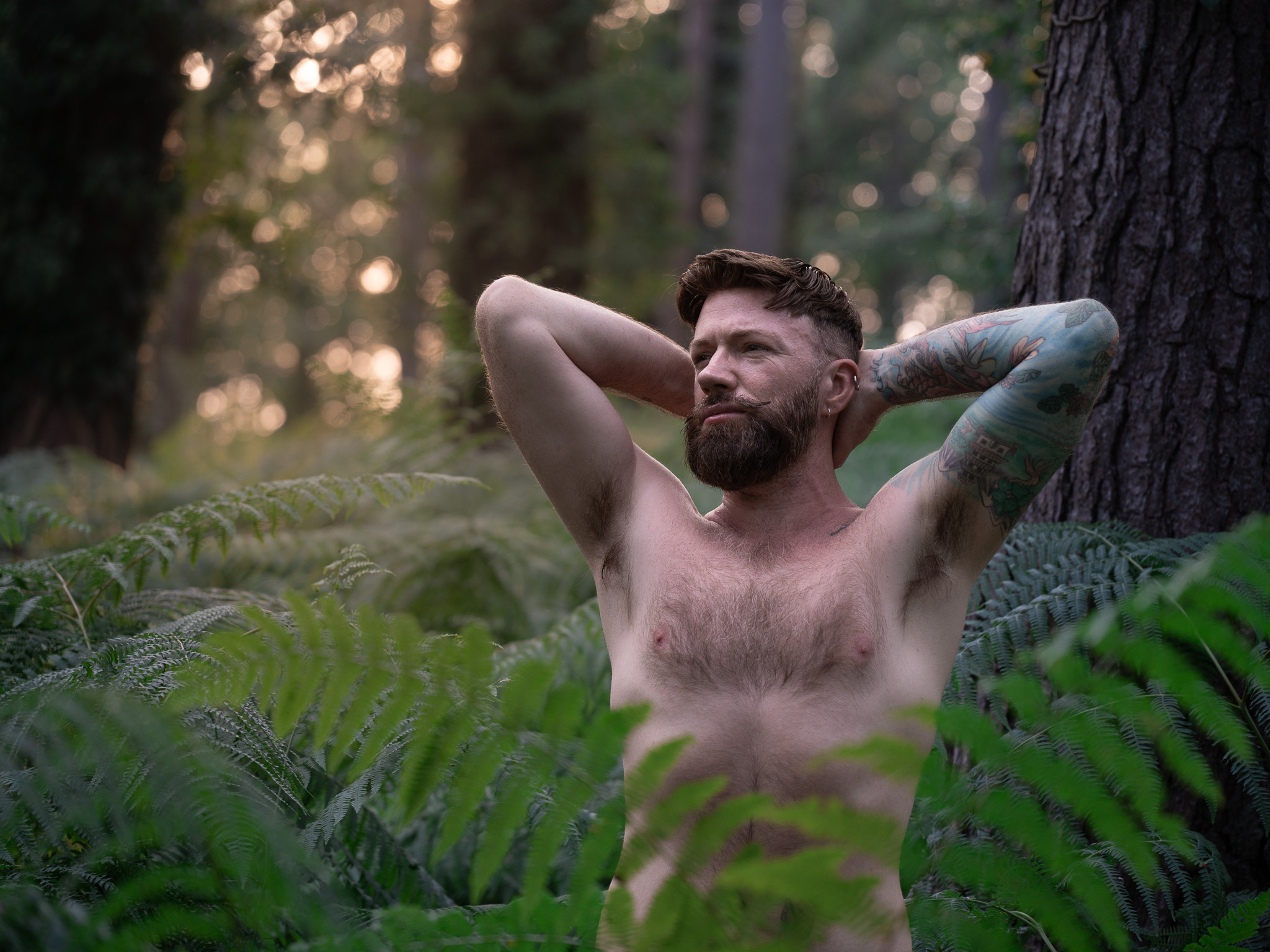 A tattooed man resting among woodland ferns
