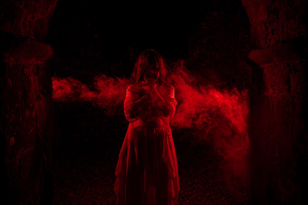 Model framed in red light and smoke within Knowlton Church ruins during a Halloween cinematic photoshoot by Studio DJC, symbolising ritual and possession.
