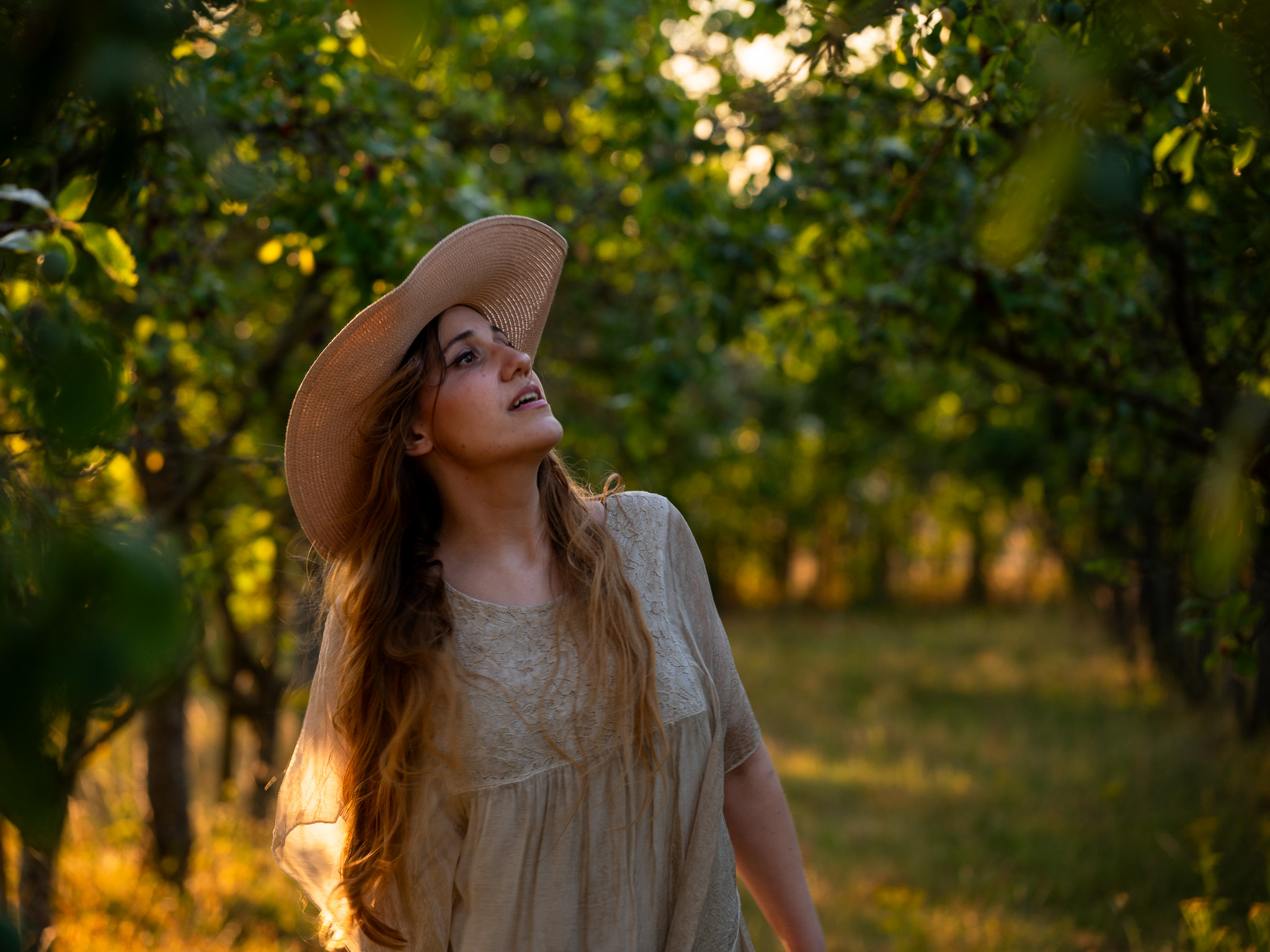 Andreea looking upwards beneath trees in warm evening light