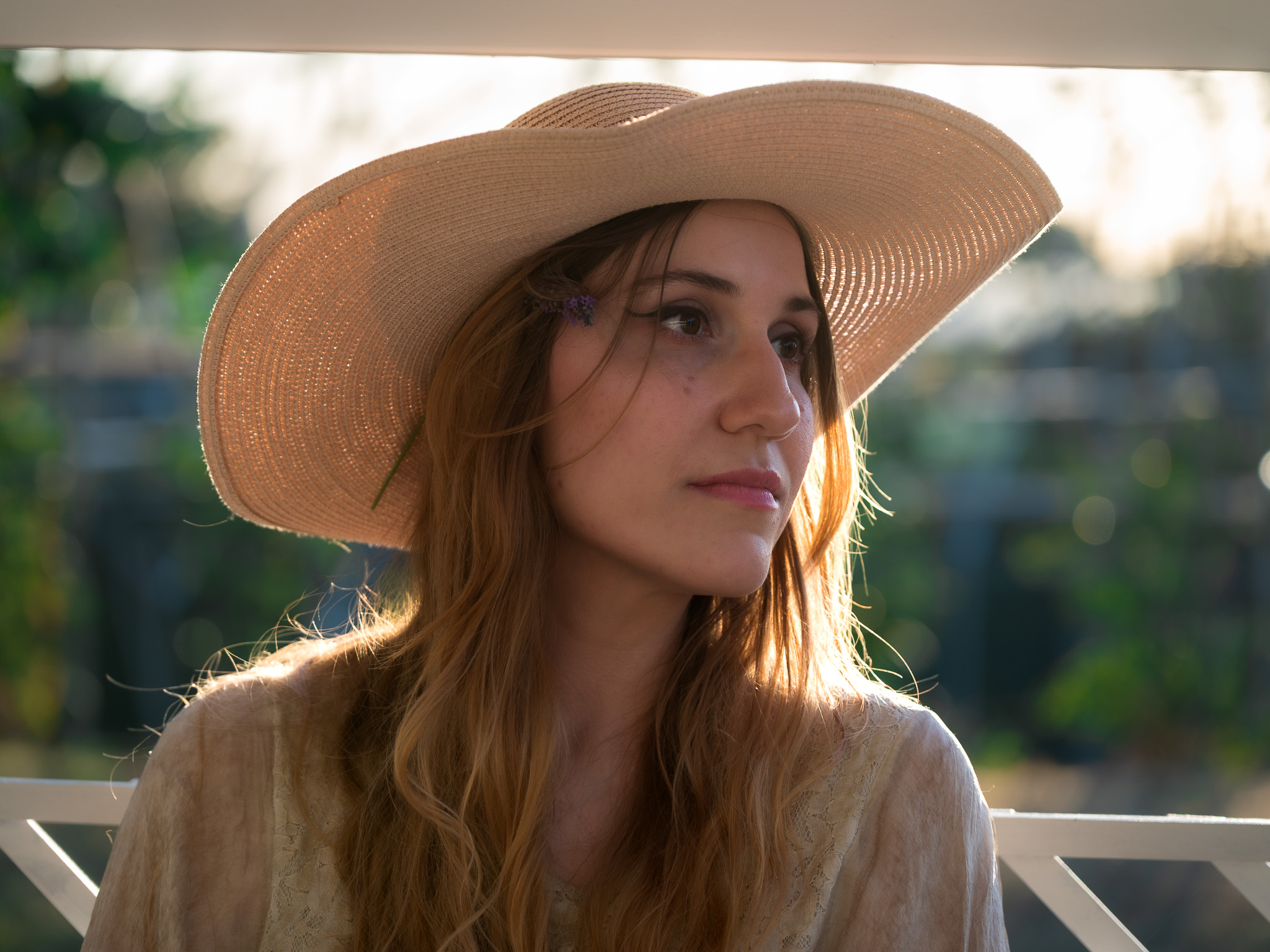 Backlit close portrait of Andreea wearing a hat with a small flower in her hair