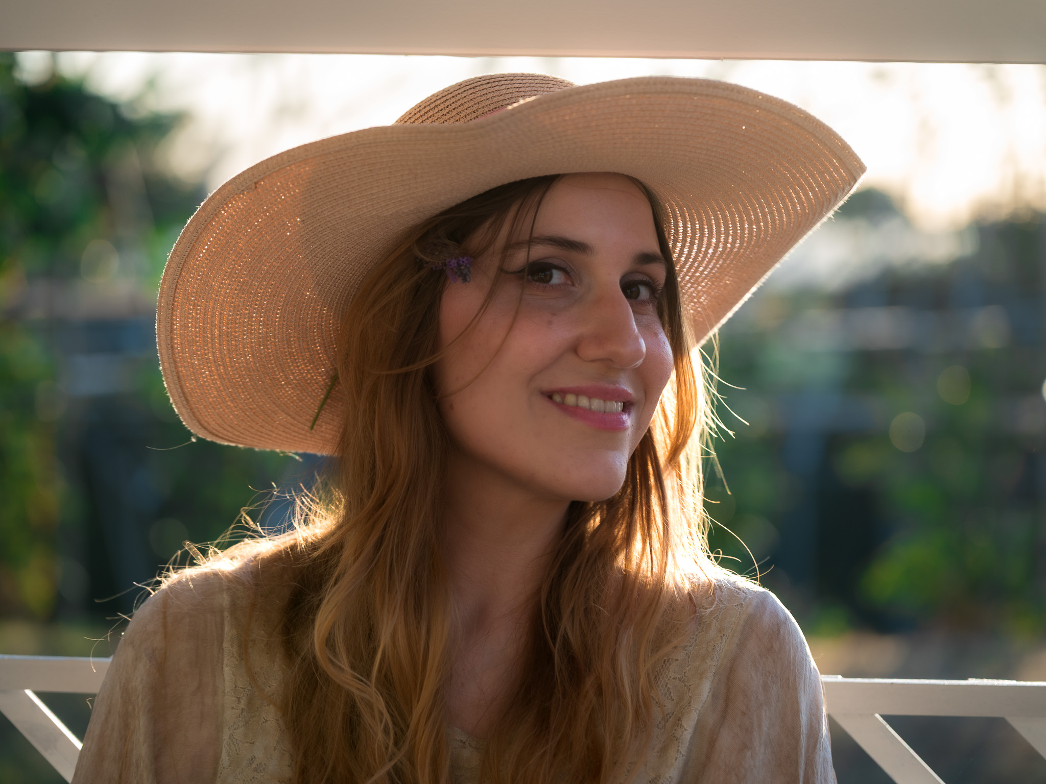 Backlit portrait of Andreea smiling beneath a wide-brimmed hat